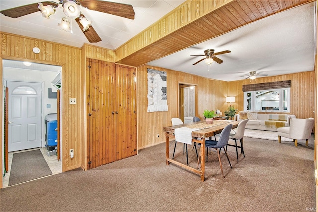 carpeted dining space with a ceiling fan and wooden walls