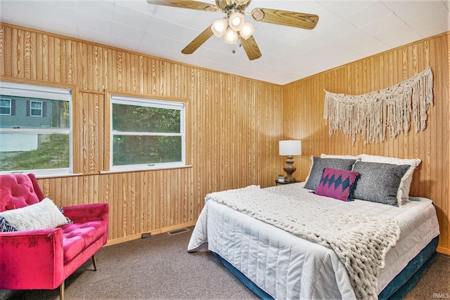 bedroom with carpet floors, ceiling fan, wooden walls, and visible vents