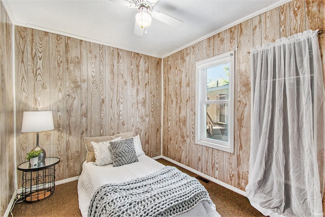 carpeted bedroom featuring wood walls, a ceiling fan, visible vents, baseboards, and ornamental molding