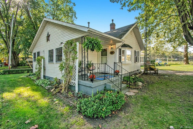 bungalow featuring covered porch, a chimney, and a front lawn