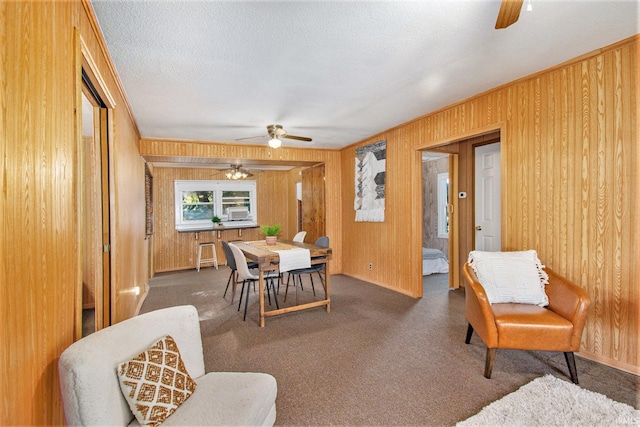 carpeted dining area with a ceiling fan, wooden walls, and a textured ceiling