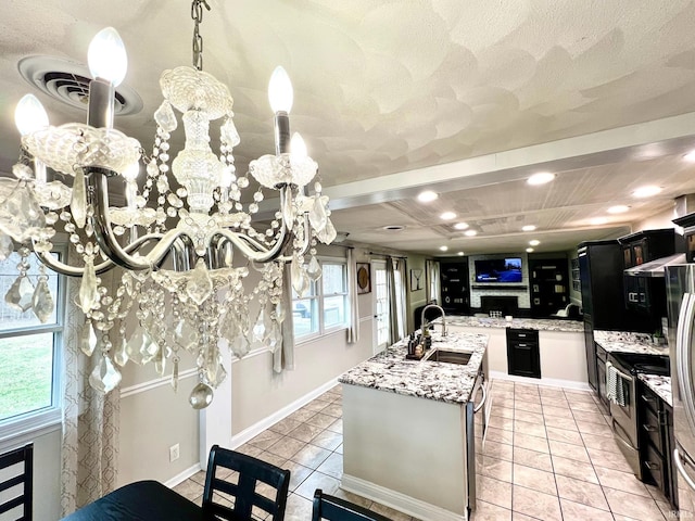 kitchen featuring light tile patterned floors, appliances with stainless steel finishes, a kitchen island with sink, a sink, and light stone countertops