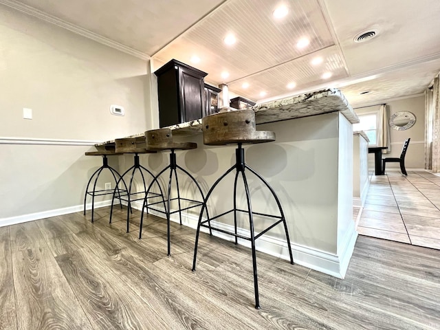 kitchen with baseboards, visible vents, wooden ceiling, a breakfast bar, and wood finished floors