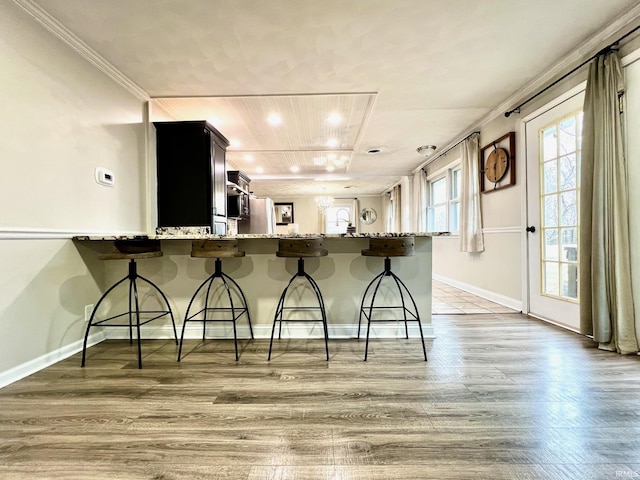 kitchen featuring light stone counters, a kitchen bar, light wood-style flooring, and baseboards