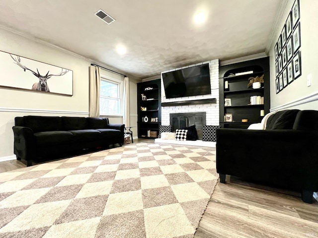 living area featuring built in shelves, visible vents, ornamental molding, a brick fireplace, and wood finished floors