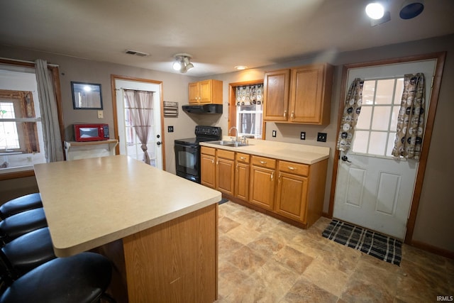 kitchen featuring black range with electric stovetop, a breakfast bar, a sink, visible vents, and light countertops