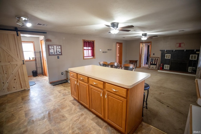 kitchen with a fireplace with raised hearth, a barn door, a kitchen island, light countertops, and a kitchen bar