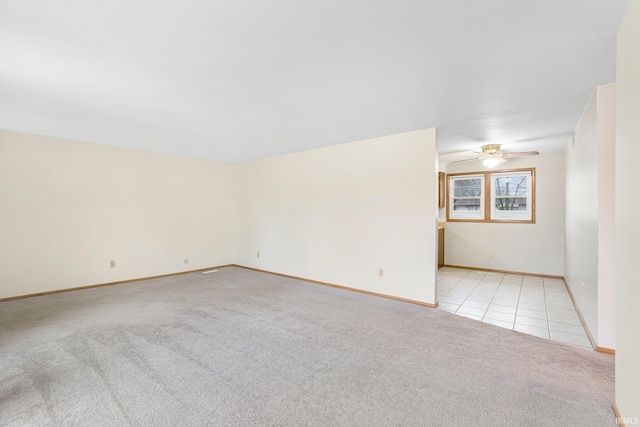 unfurnished room with light carpet, light tile patterned floors, ceiling fan, and baseboards