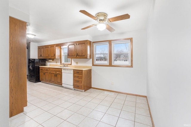 kitchen with brown cabinets, light countertops, a sink, dishwasher, and baseboards