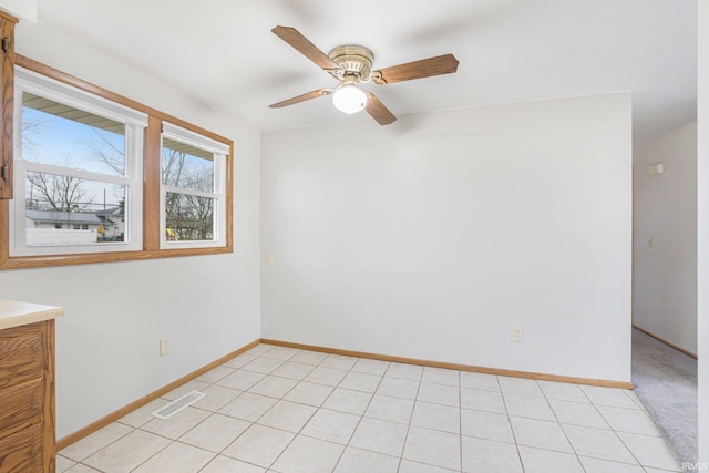 empty room featuring a ceiling fan, visible vents, baseboards, and light tile patterned floors