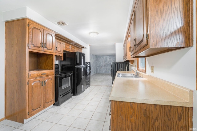 kitchen featuring washing machine and dryer, a sink, visible vents, black appliances, and brown cabinetry