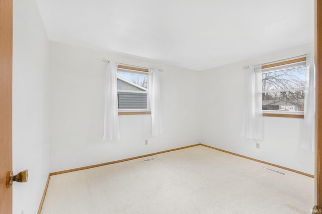 carpeted spare room featuring plenty of natural light, visible vents, and baseboards