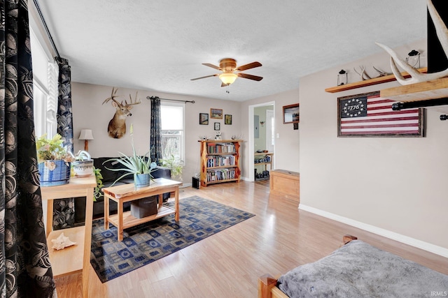 living area featuring a ceiling fan, a textured ceiling, baseboards, and wood finished floors