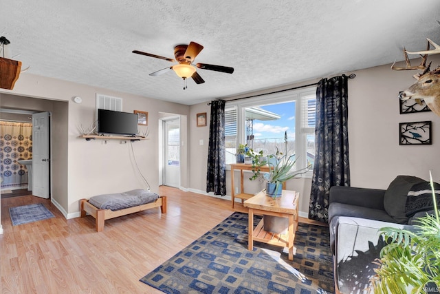 living room featuring a textured ceiling, ceiling fan, visible vents, baseboards, and light wood-style floors