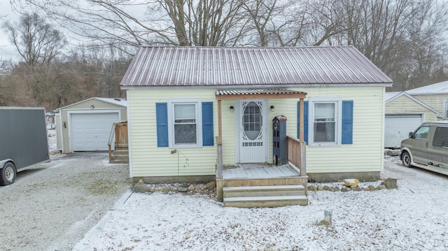 bungalow-style home featuring driveway, a detached garage, metal roof, and an outbuilding