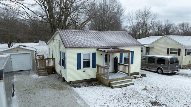 bungalow with driveway, a detached garage, metal roof, and an outbuilding