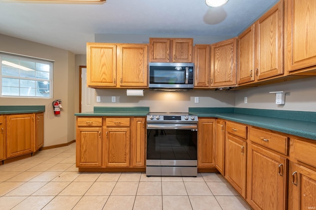 kitchen with light tile patterned floors, stainless steel appliances, baseboards, and brown cabinetry