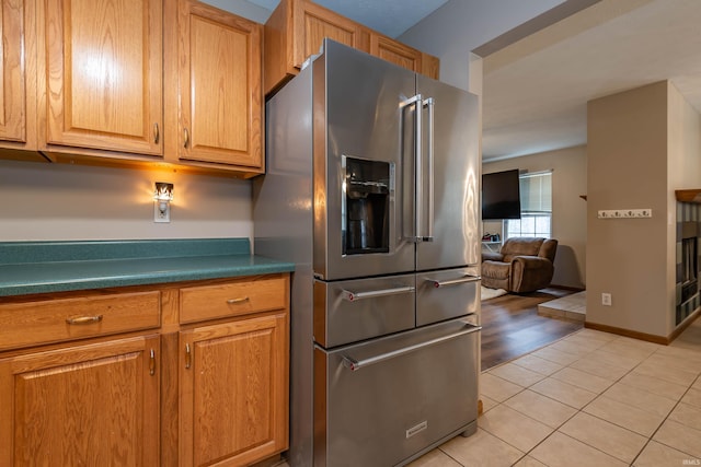 kitchen featuring brown cabinets, high end fridge, dark countertops, light tile patterned floors, and baseboards