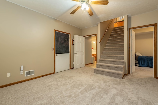 below grade area with visible vents, baseboards, stairs, light carpet, and a ceiling fan