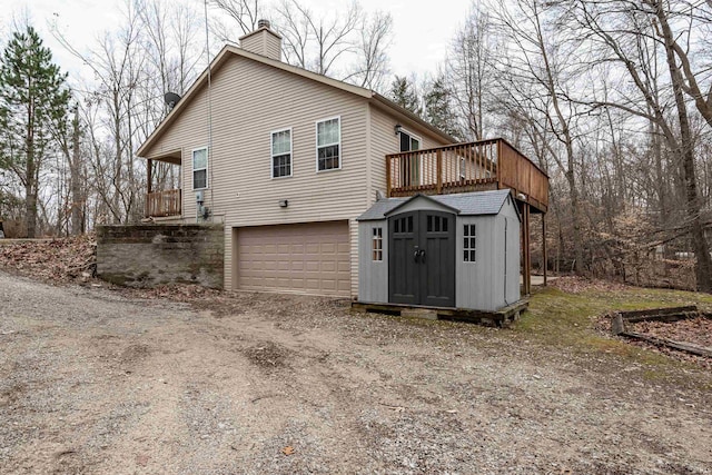 view of home's exterior featuring a storage unit, an outbuilding, driveway, an attached garage, and a chimney