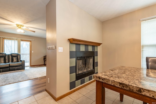 interior space featuring light tile patterned floors, baseboards, a ceiling fan, and a fireplace