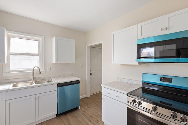 kitchen with stainless steel appliances, light countertops, white cabinets, a sink, and light wood-type flooring