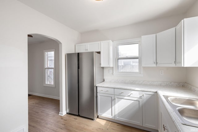 kitchen featuring arched walkways, light wood-style flooring, a sink, white cabinetry, and freestanding refrigerator