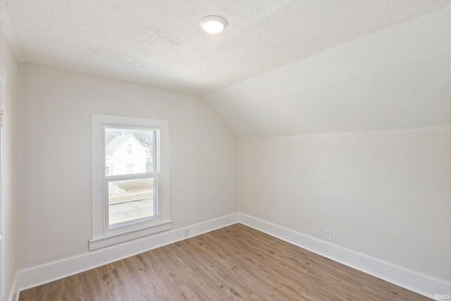 bonus room featuring light wood-style floors, vaulted ceiling, a textured ceiling, and baseboards