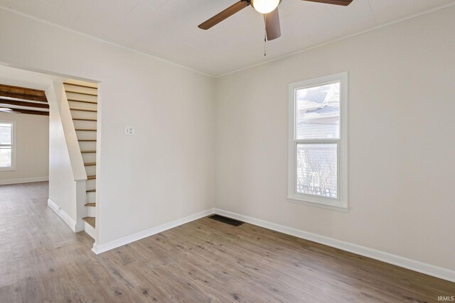 spare room with ceiling fan, wood finished floors, visible vents, baseboards, and stairs