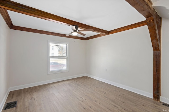 spare room with visible vents, a ceiling fan, ornamental molding, light wood-type flooring, and baseboards