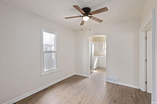 unfurnished room with arched walkways, ceiling fan, light wood-style flooring, visible vents, and baseboards