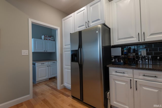 kitchen with decorative backsplash, stainless steel fridge with ice dispenser, light wood-style flooring, dark stone countertops, and white cabinetry