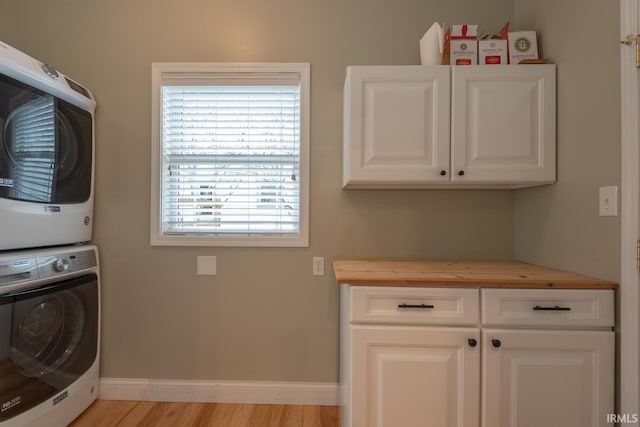 clothes washing area with stacked washer / dryer, cabinet space, light wood-style flooring, and baseboards