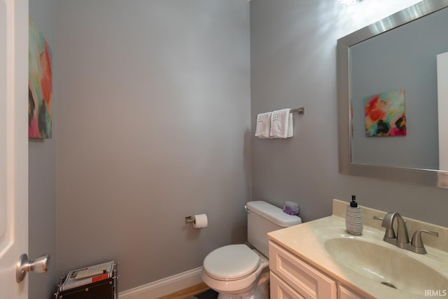 half bath featuring baseboards, vanity, and toilet