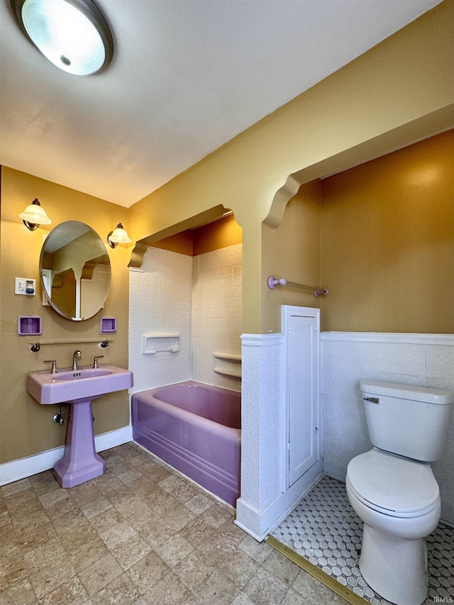 bathroom with a tub, wainscoting, and toilet