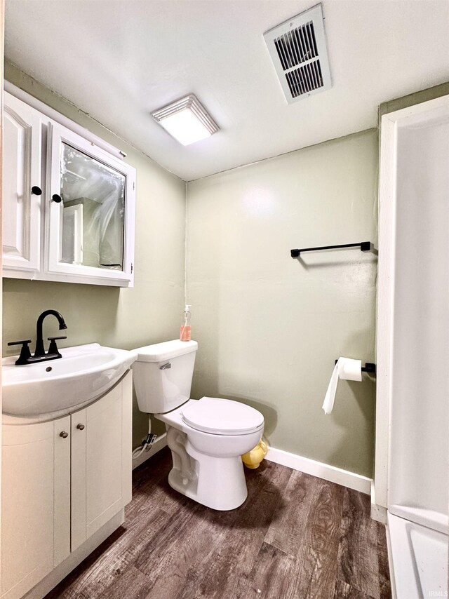 half bathroom featuring toilet, vanity, wood finished floors, and visible vents