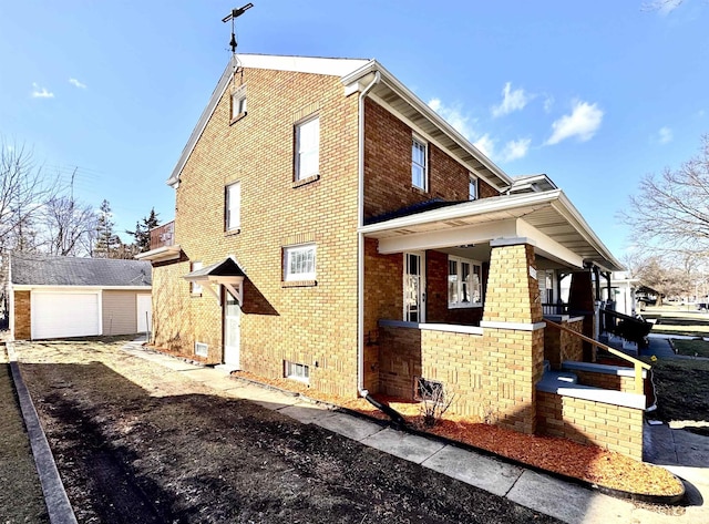 view of property exterior with an outbuilding, aphalt driveway, covered porch, brick siding, and a detached garage