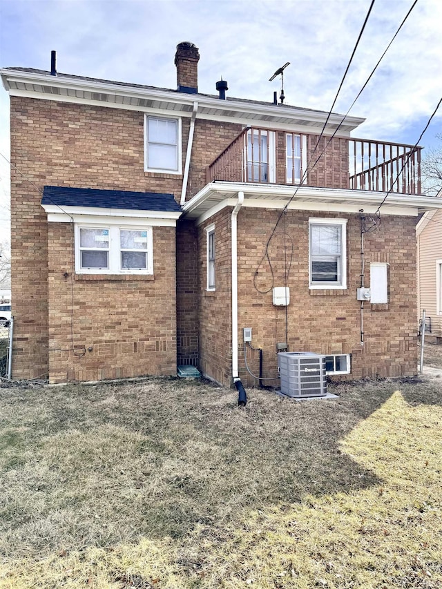 rear view of property with a yard, brick siding, a chimney, and a balcony