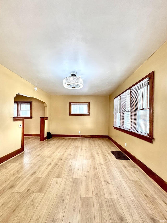 spare room featuring light wood-style floors, baseboards, visible vents, and arched walkways