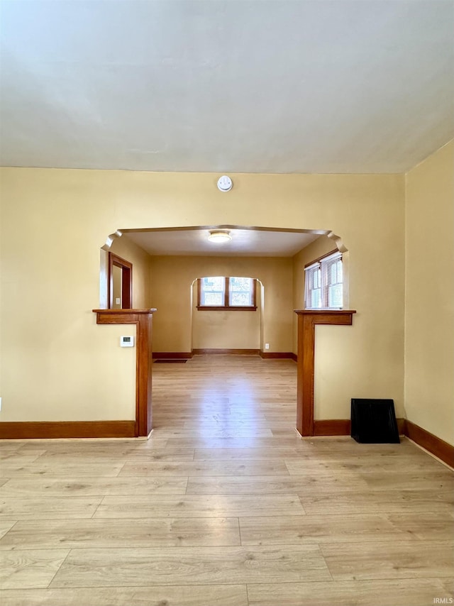 spare room featuring arched walkways, light wood-style flooring, and baseboards