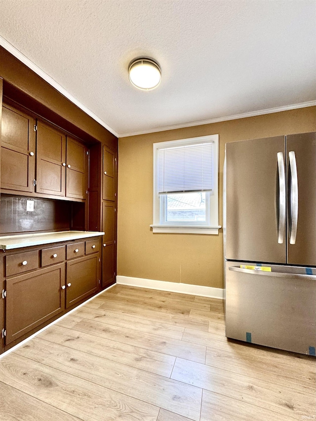 kitchen with light wood-type flooring, freestanding refrigerator, a textured ceiling, and baseboards