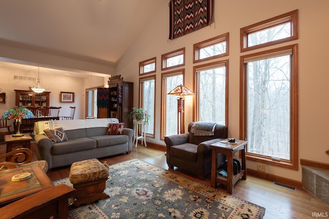 living area with high vaulted ceiling, wood finished floors, visible vents, and baseboards