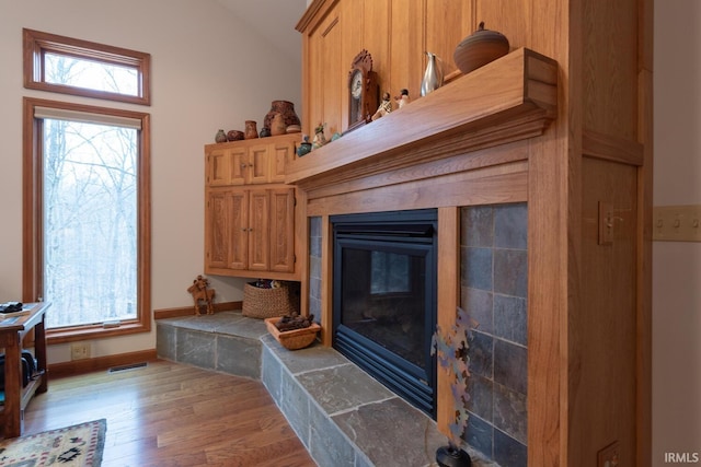 interior details with a tile fireplace, wood finished floors, visible vents, and baseboards