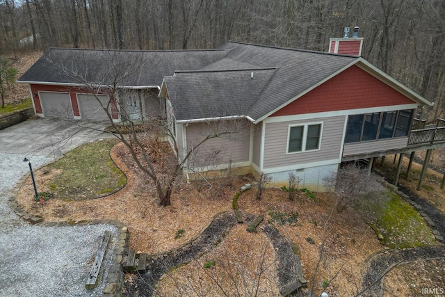 view of front of house with a shingled roof, concrete driveway, a sunroom, a chimney, and crawl space