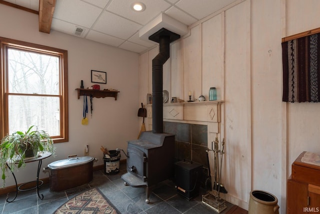 interior space with a wood stove, visible vents, baseboards, and a drop ceiling