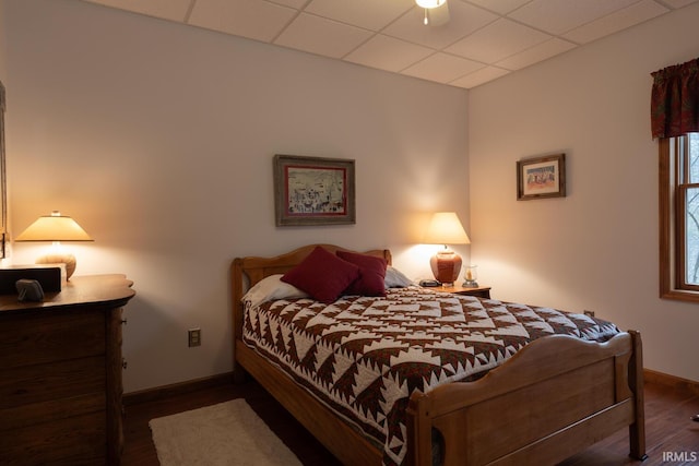 bedroom featuring a drop ceiling, baseboards, and wood finished floors