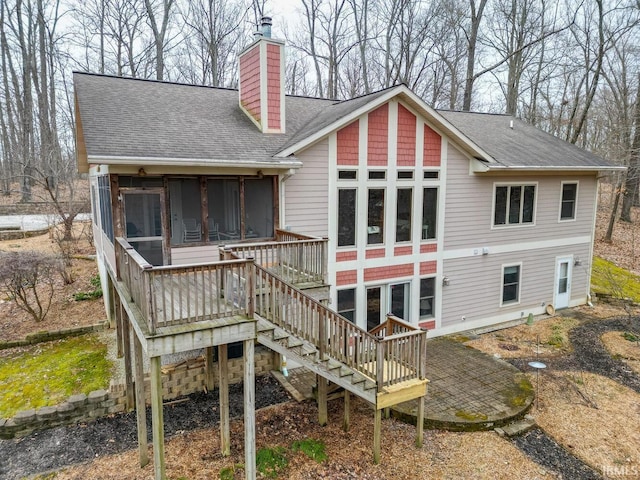 rear view of property with a shingled roof, a sunroom, a chimney, stairway, and a wooden deck