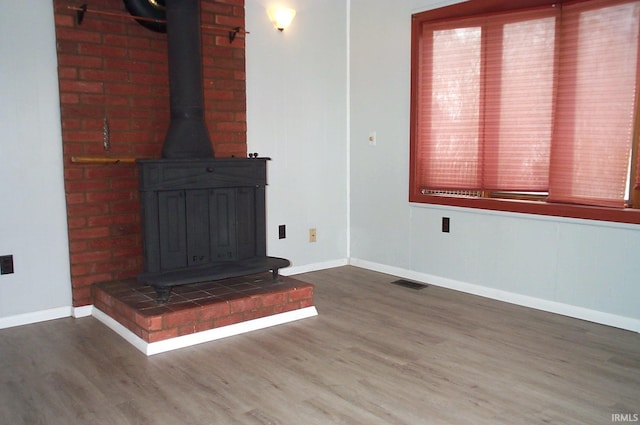 unfurnished living room featuring a wood stove, baseboards, visible vents, and wood finished floors