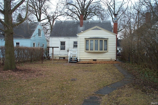 back of property with entry steps, a shingled roof, a lawn, a chimney, and crawl space