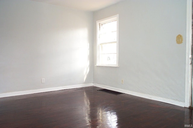 empty room featuring dark wood-style flooring, visible vents, and baseboards